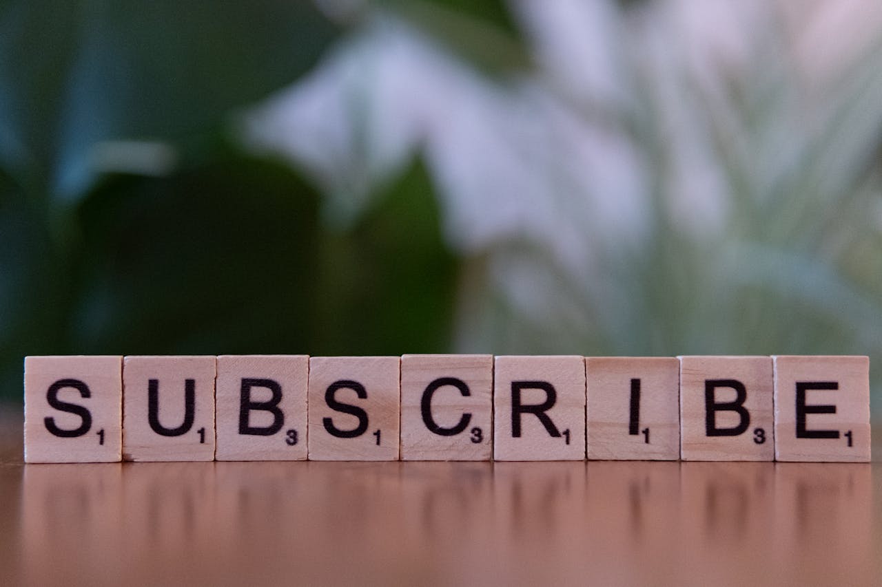 Close-up of the word SUBSCRIBE spelled with wooden letter tiles on a table.
